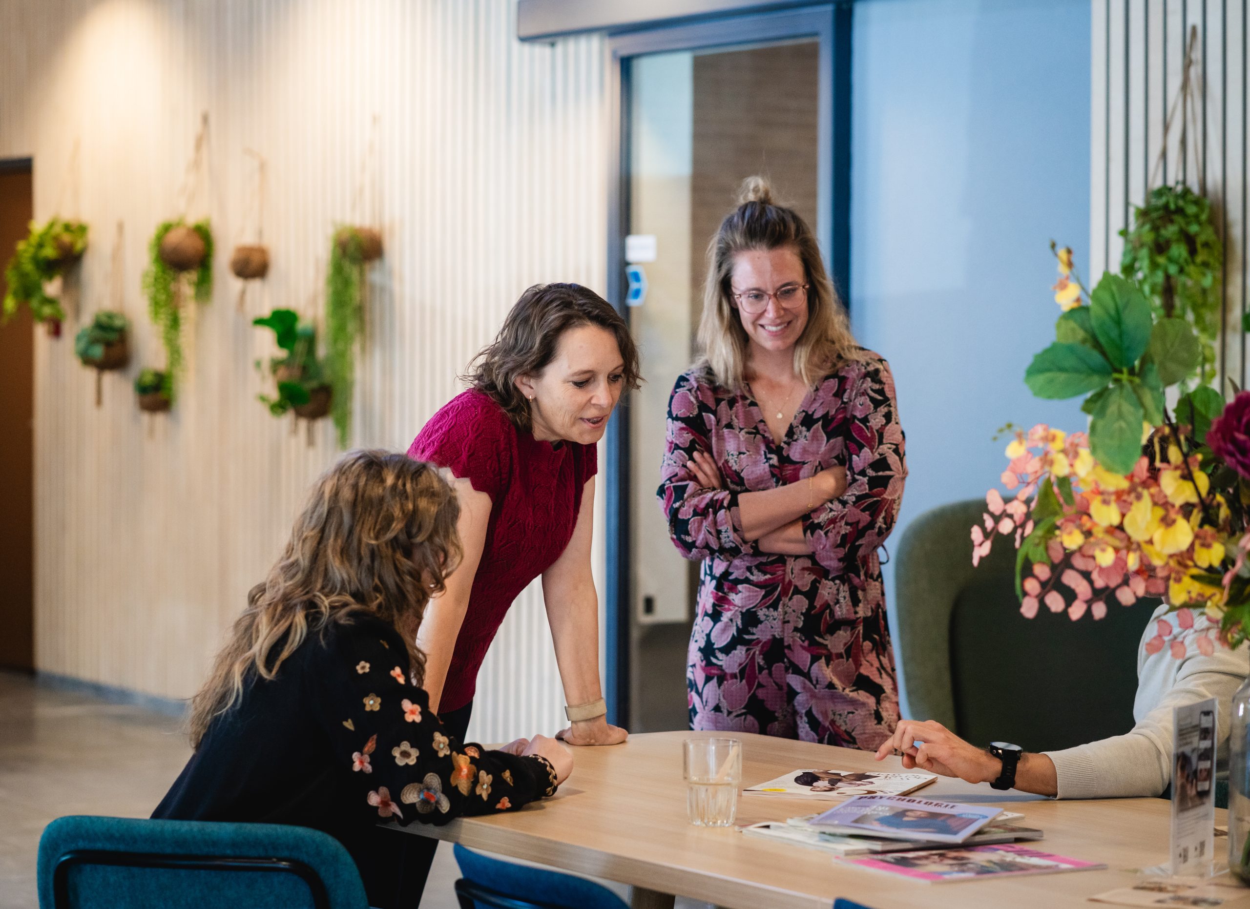 Drie vrouwen in werkkleding rondom een tafel. Twee staan, één zit. Ze hebben duidelijk een actieve houding.